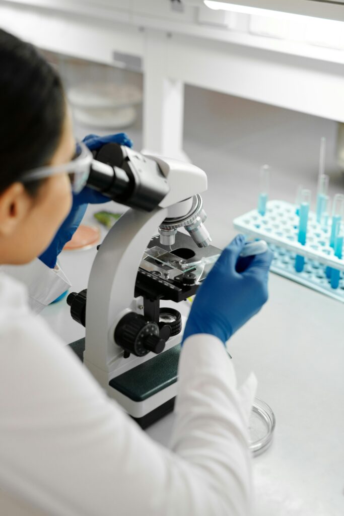 A scientist examines a sample under a microscope in a laboratory setting, wearing protective gear.