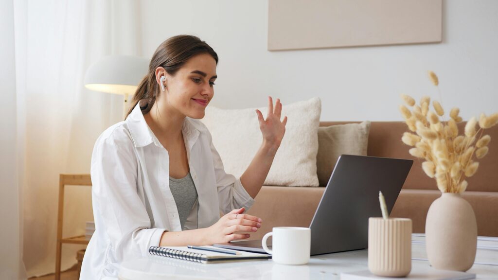 Cheerful young woman using laptop for a video call in a cozy living room, feeling connected and happy.