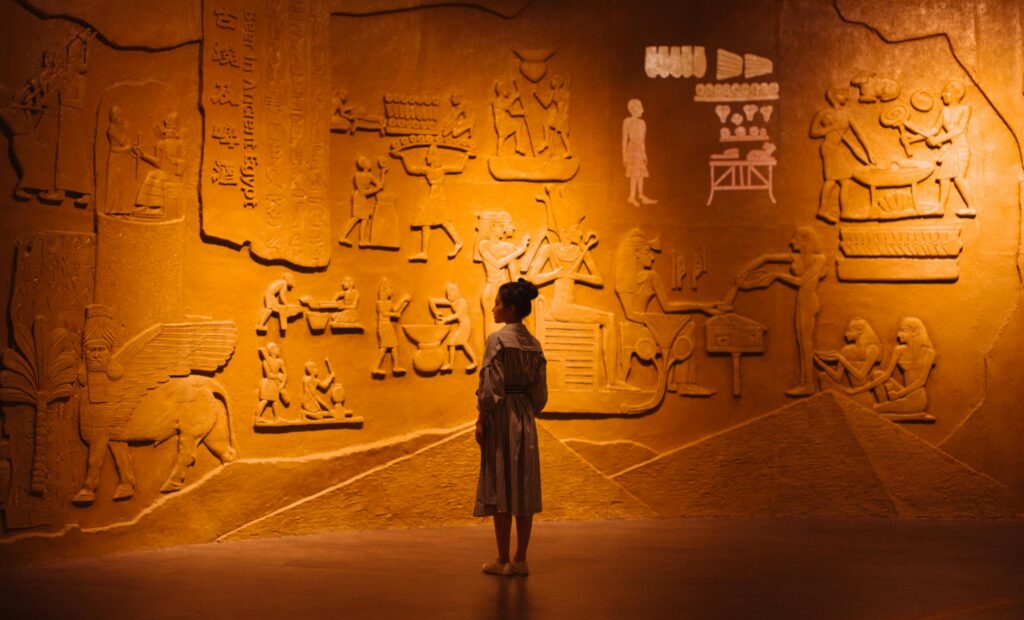 Back view of anonymous female traveler standing near ancient wall with Egyptian engraving