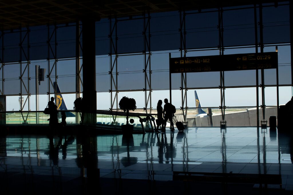 Travelers silhouetted in a modern airport terminal with glass windows and visible airplane tails.