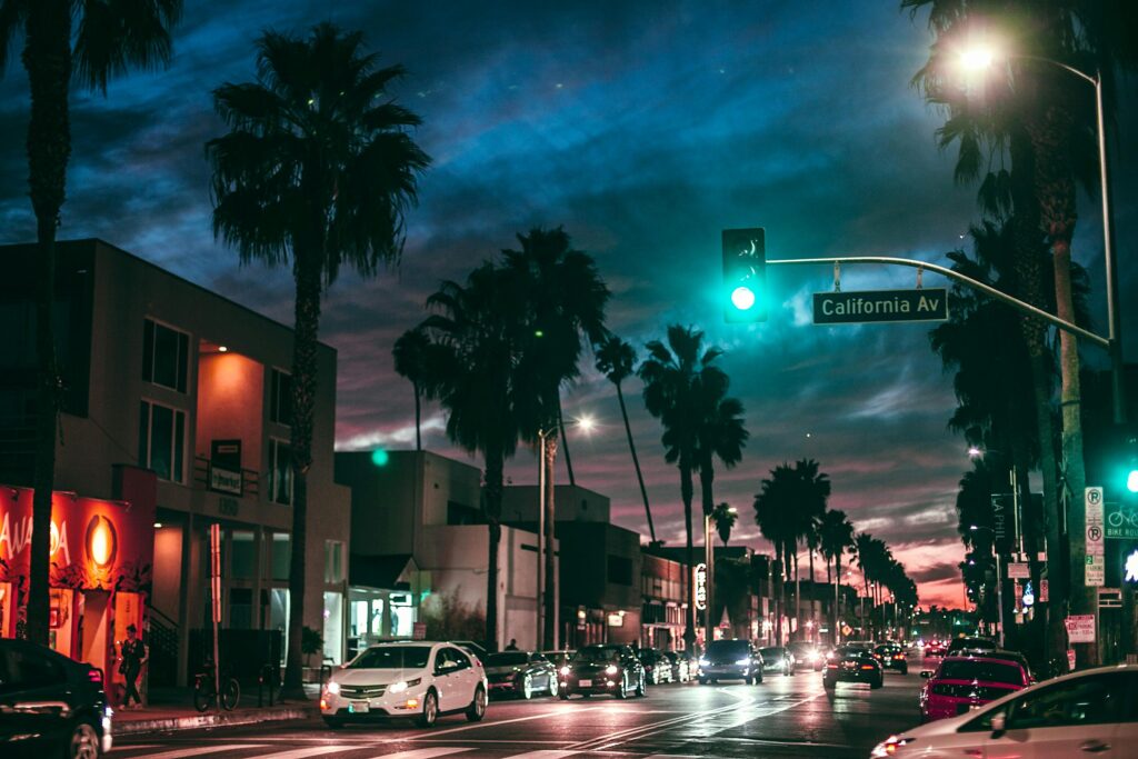 A bustling night scene featuring cars and palm trees on California Avenue, illuminated by streetlights.