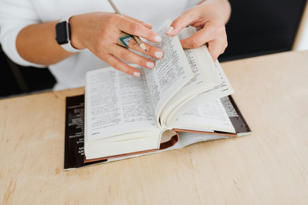 A close-up of a woman turning the pages of a dictionary on a wooden desk.