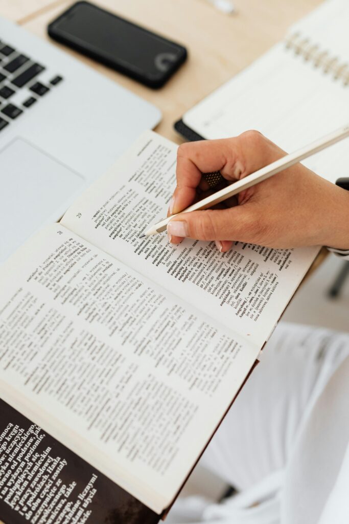 Close-up of a person underlining text in a dictionary on a desk with a laptop.