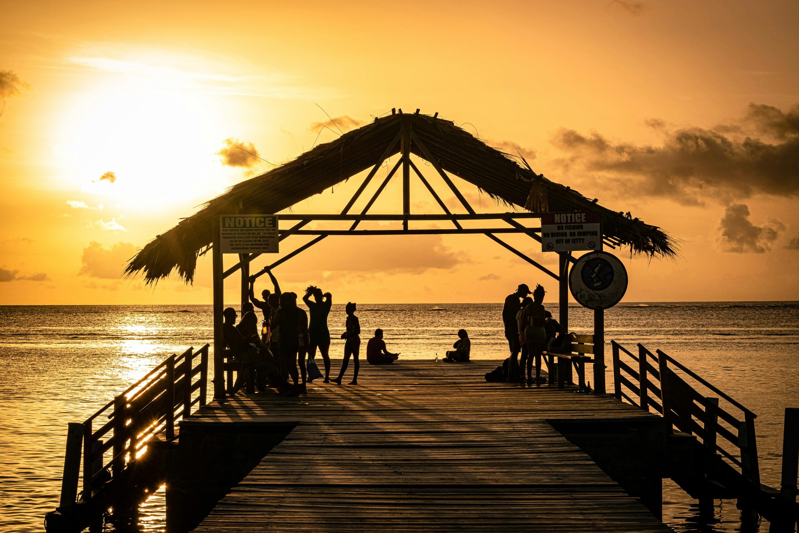 Silhouetted people gather on a tropical jetty during a breathtaking sunset in Western Tobago.