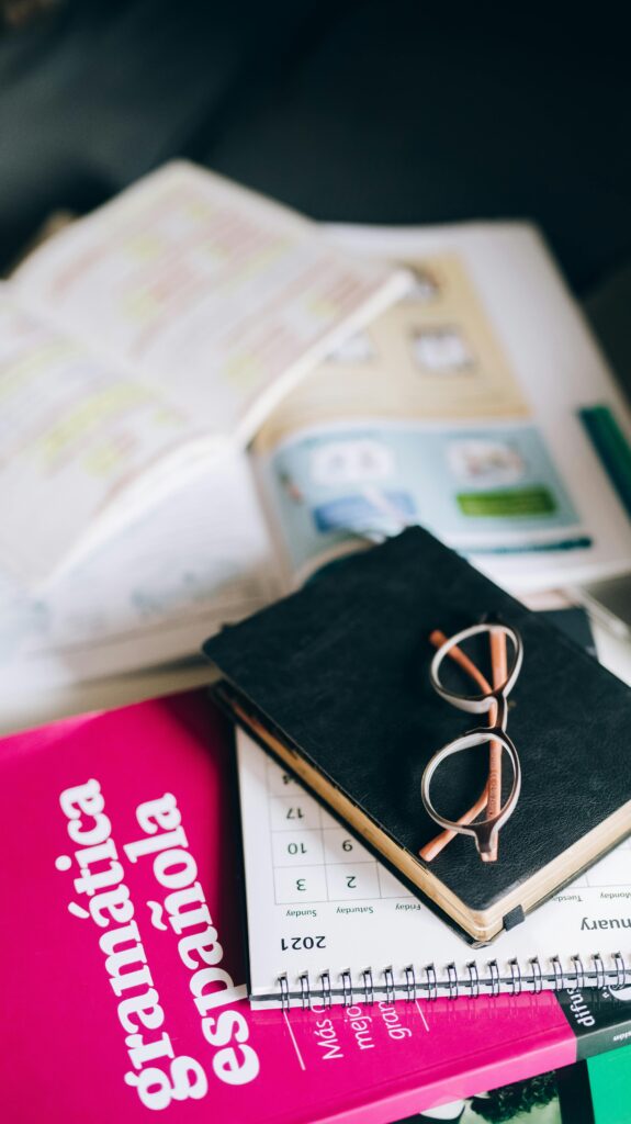 A study setup with a Spanish grammar book, calendar, and eyeglasses on a desk, suggesting focused learning.