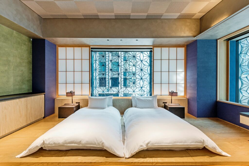 A modern hotel room featuring twin beds, Japanese design elements, and wooden flooring.