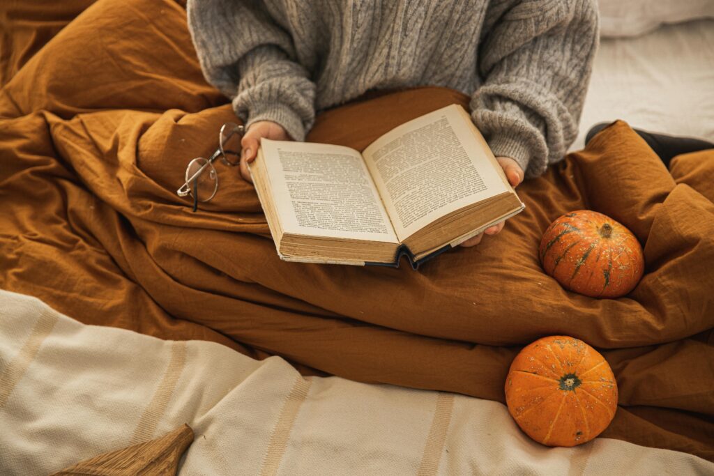 A person reading a book in a cozy setting with pumpkins, embodying autumn relaxation.