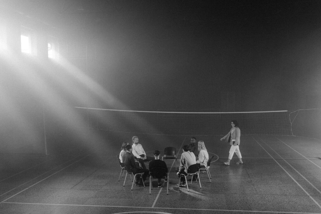 A black and white image of a small group therapy session in a smoky indoor sports hall.