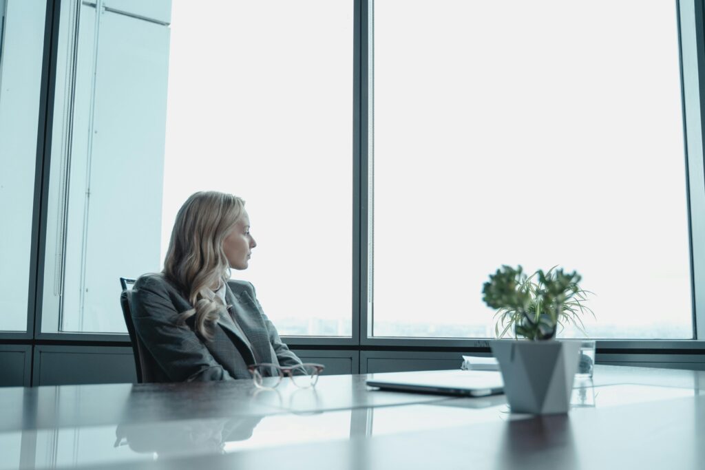 A businesswoman in a suit looking out the window of a contemporary office with a modern setup.