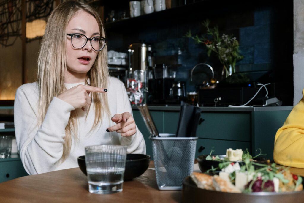 Woman using sign language while dining at a café, with focus on gesture communication.