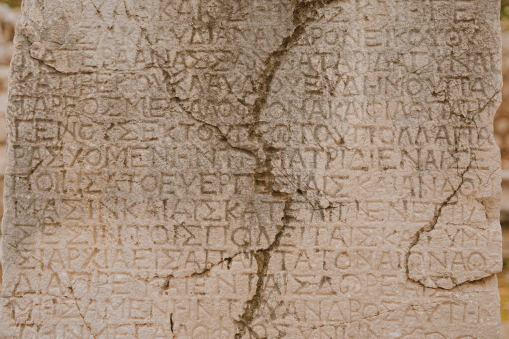 Close-up of a weathered stone with ancient Greek letters inscribed, showcasing historical text.