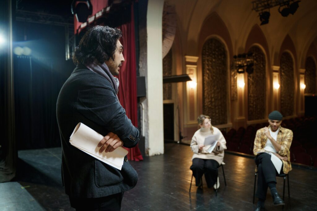 Actors rehearsing on stage in a vintage theater auditorium with a director observing.