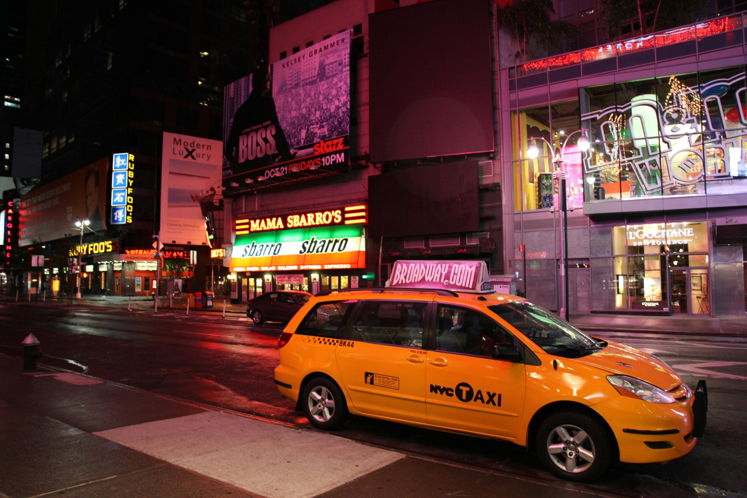 Yellow NYC taxi cab parked in vibrant Times Square, New York City streets at night.