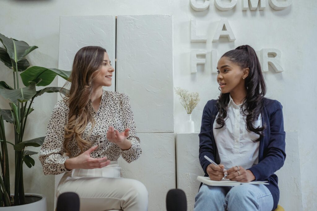 Two women having a lively interview indoors with plants and decor in the background.