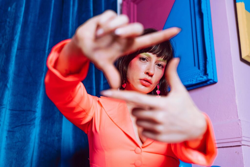 A vibrant portrait of a woman with colorful makeup, framed in a creative pose, indoors.