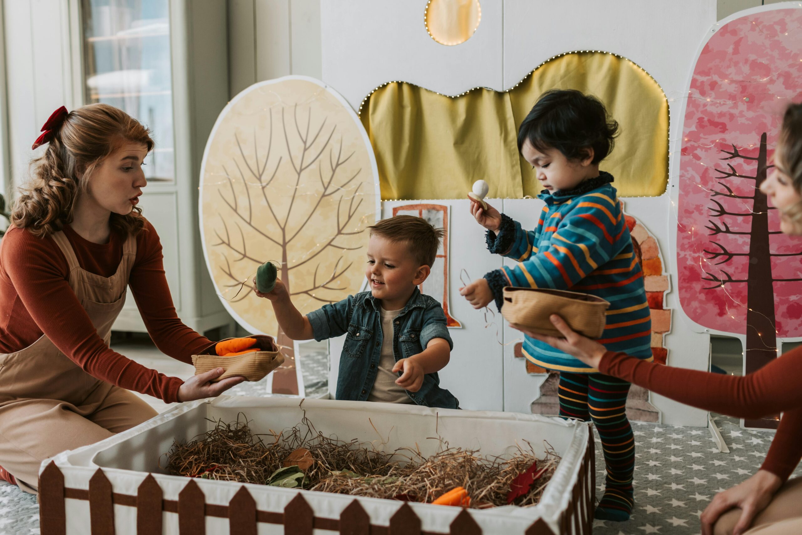 Two children and a woman play with puppets indoors, enjoying creative play with nature-themed decor.