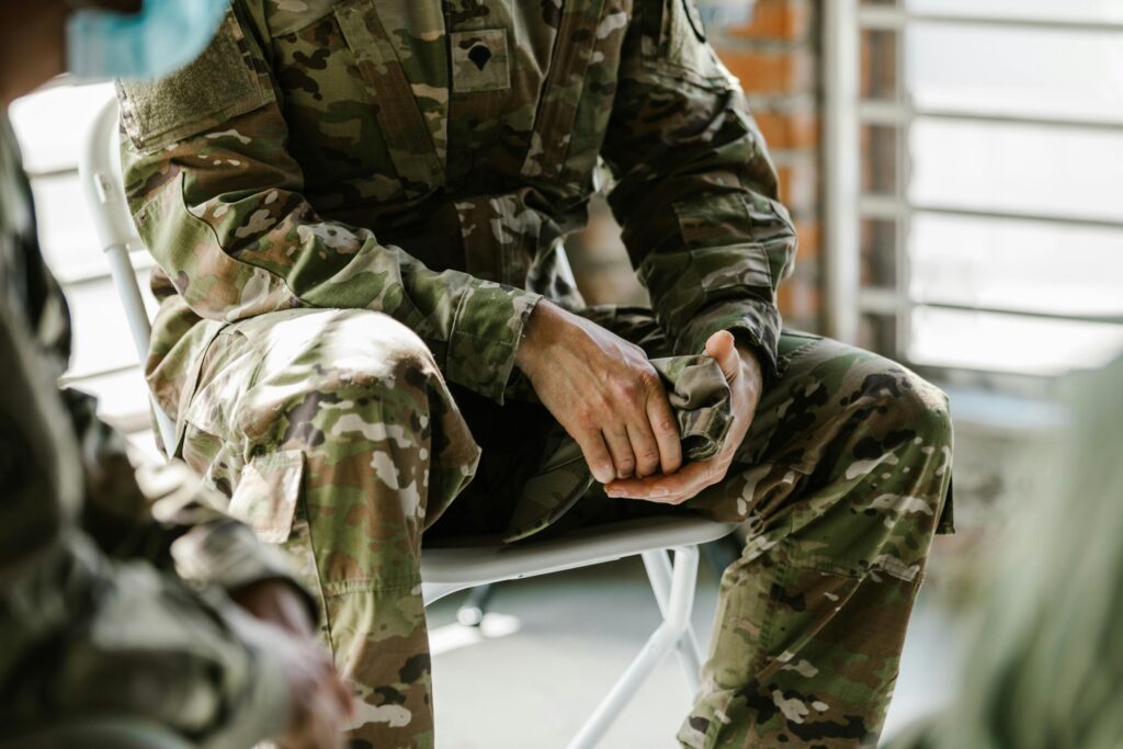 A soldier in camouflage uniform sitting indoors, representing military life and service.