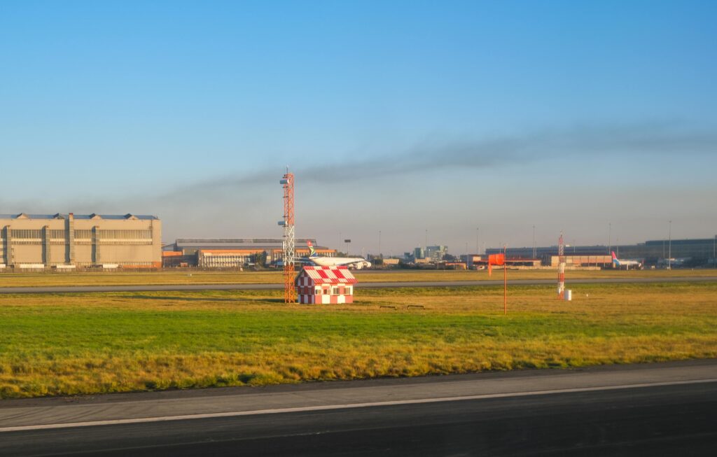 Sunny day at an airport runway, showcasing hangars and clear blue sky.