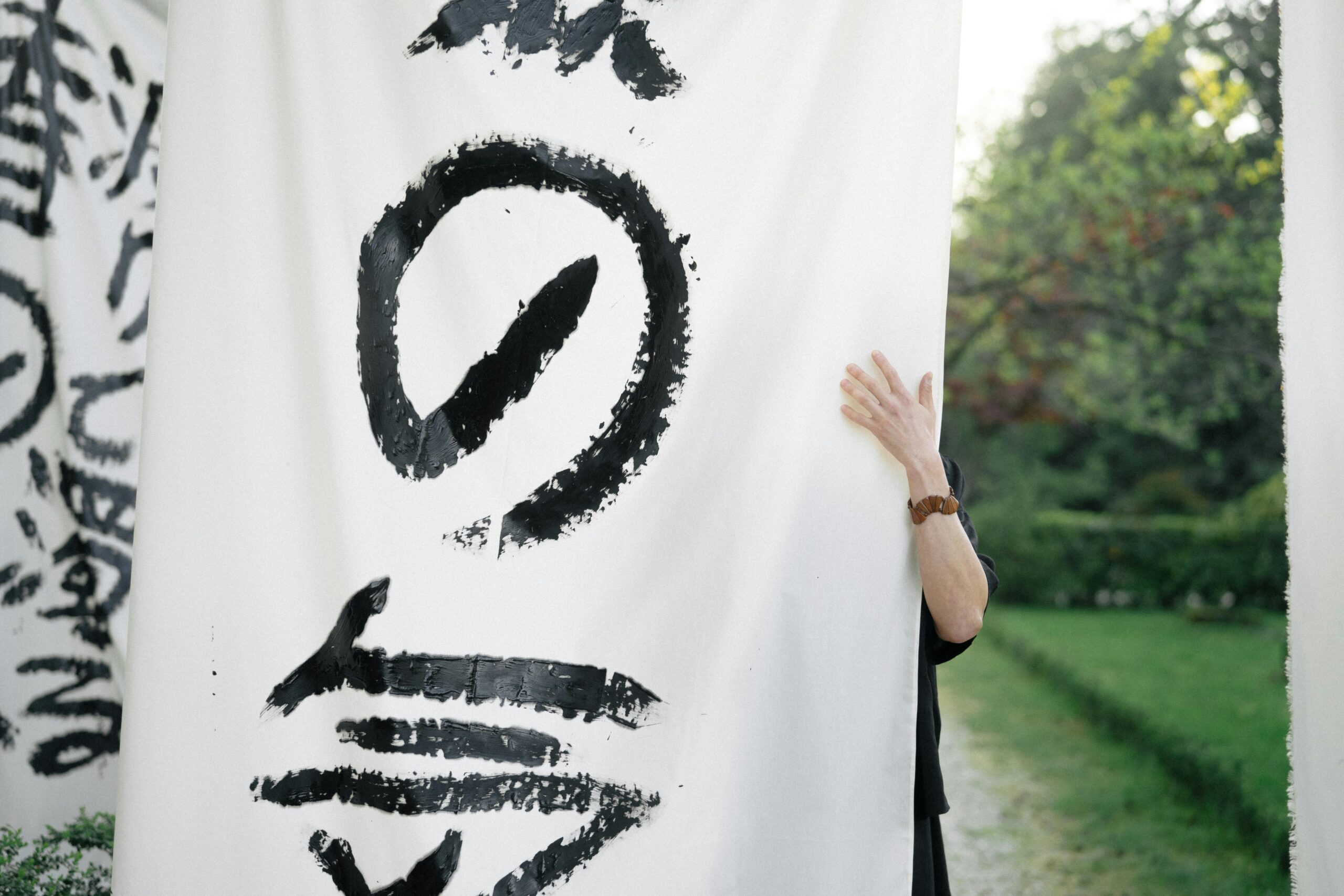 An individual holds a Japanese calligraphy banner in an outdoor garden setting.