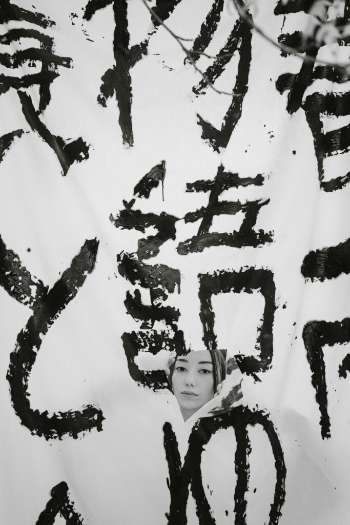 Black ink Japanese calligraphy with a woman's face peeking through, artistic and abstract.