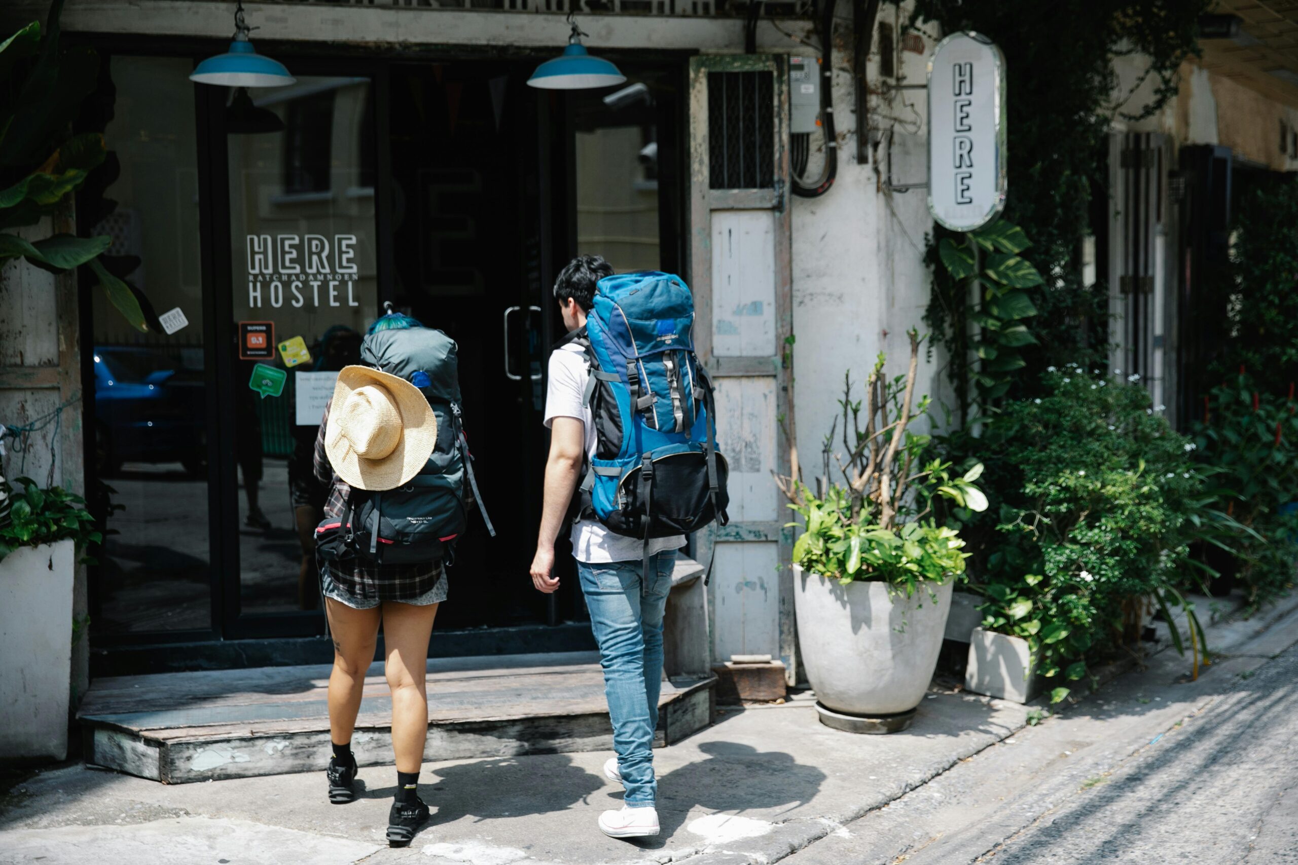 Two backpackers entering a hostel on a sunny day, exploring urban travel.