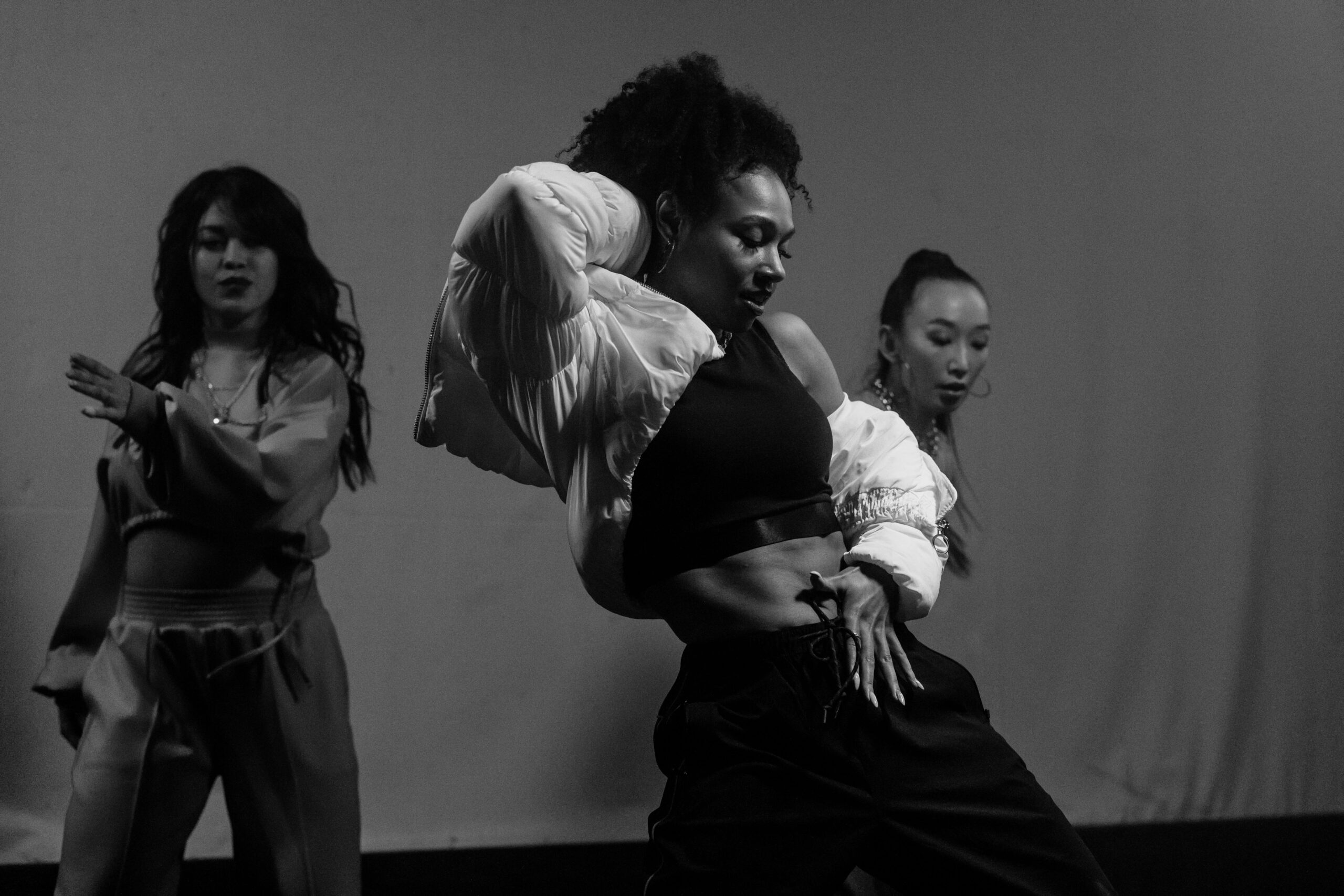 Black and white photo of a group of women performing expressive hip hop dance indoors.