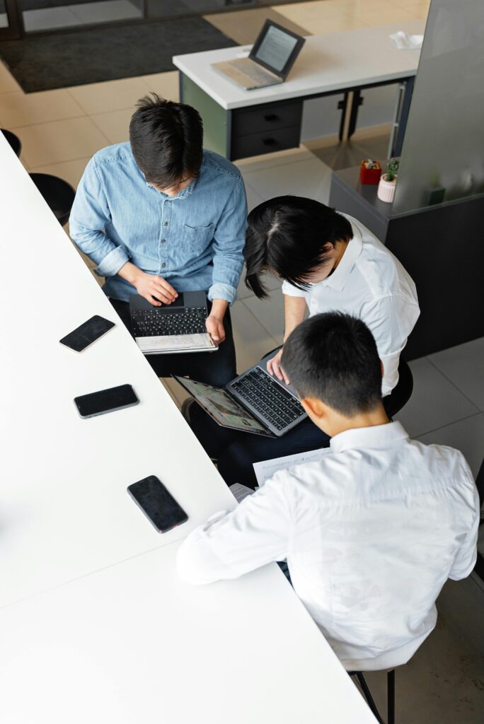 Three colleagues working together at laptops in a modern office setting, viewed from above.