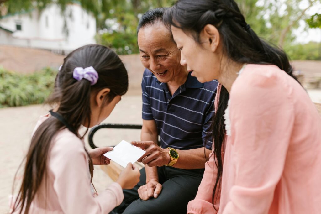 Three Asian family members enjoying quality time together with a card outdoors.