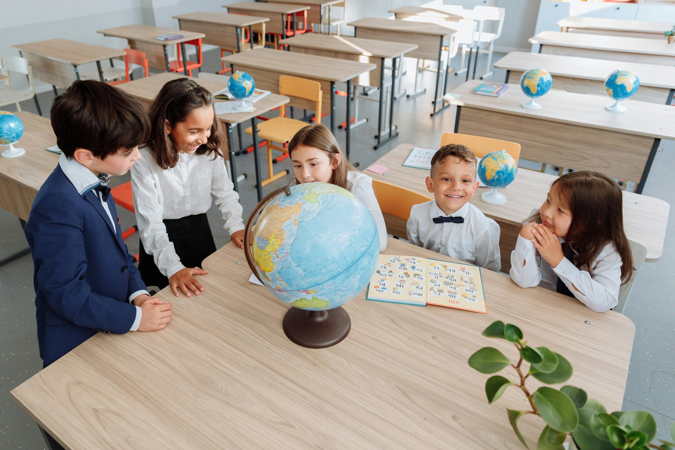 Group of children learning about geography using a globe in a bright classroom setting.