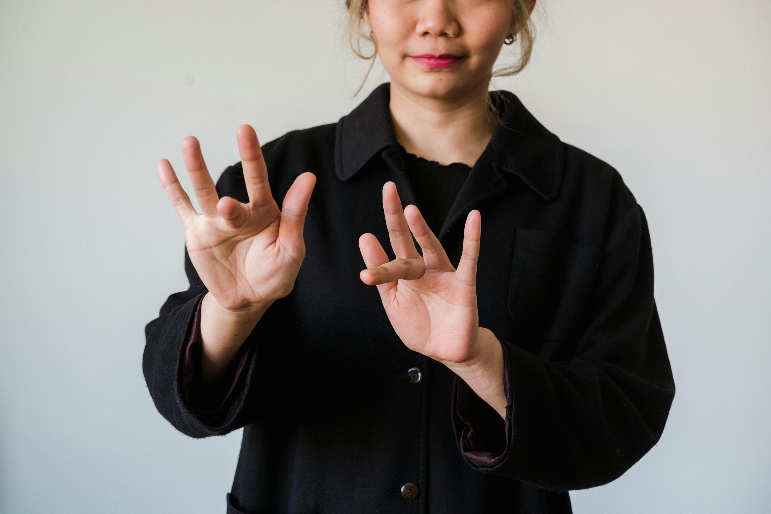 Woman demonstrating sign language on a white background, highlighting hand gestures and communication.