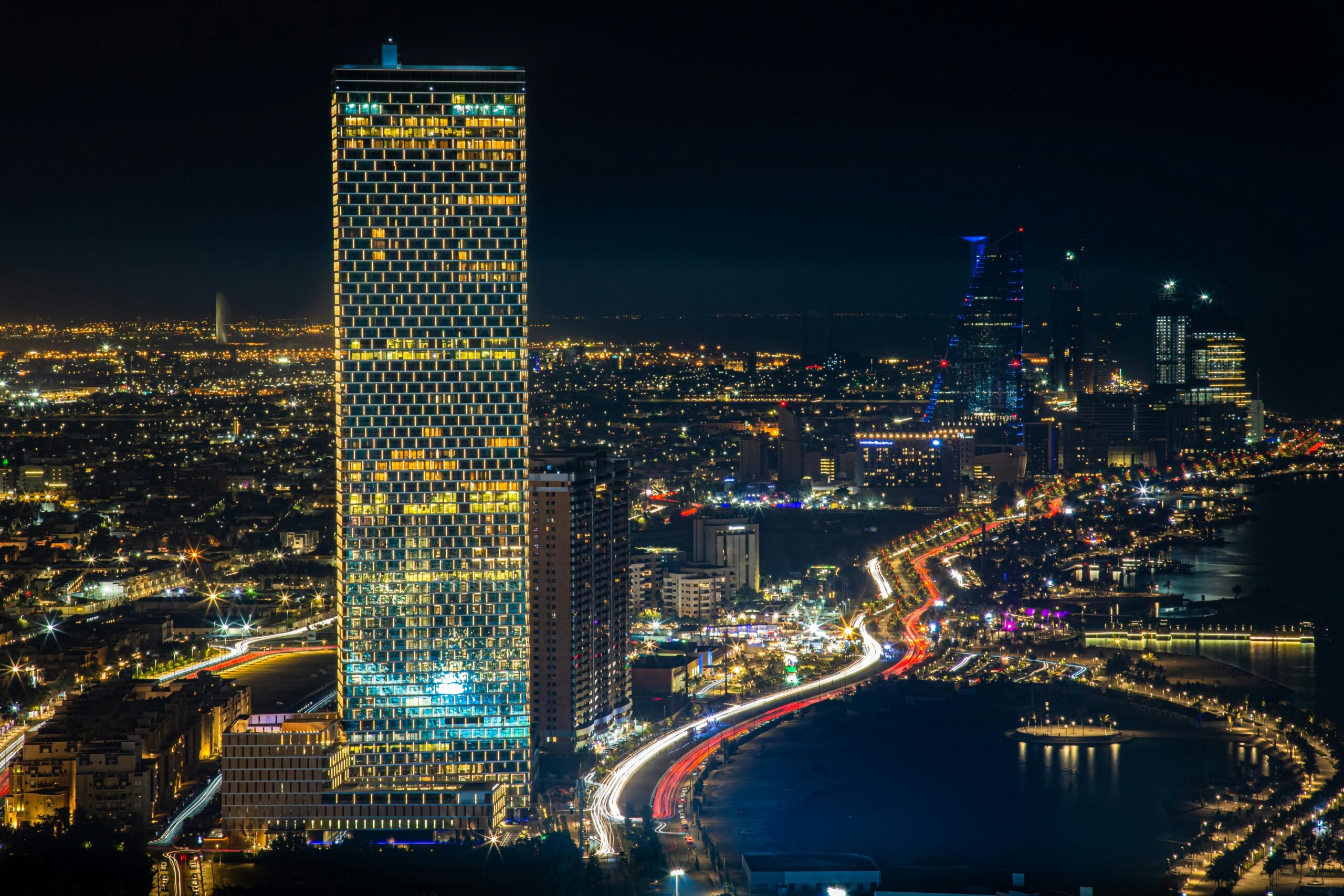 Capture the essence of Jeddah's vibrant cityscape with glowing skyscrapers and bustling streets at night.