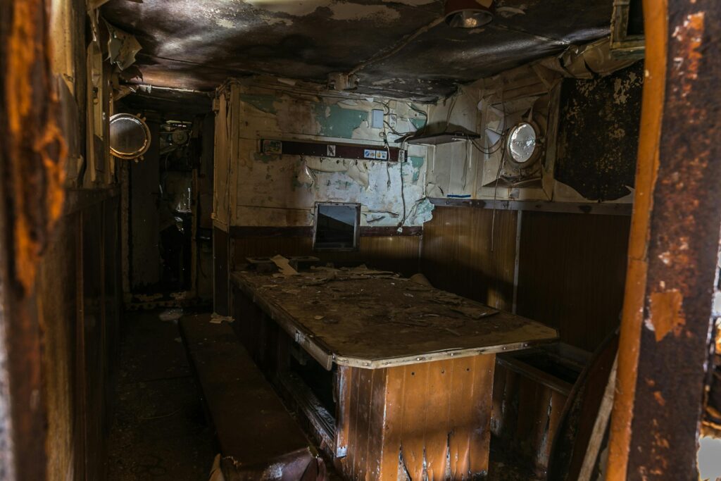 Explore the eerie and decayed interior of an abandoned ship's cabin with peeling walls and a wooden table.