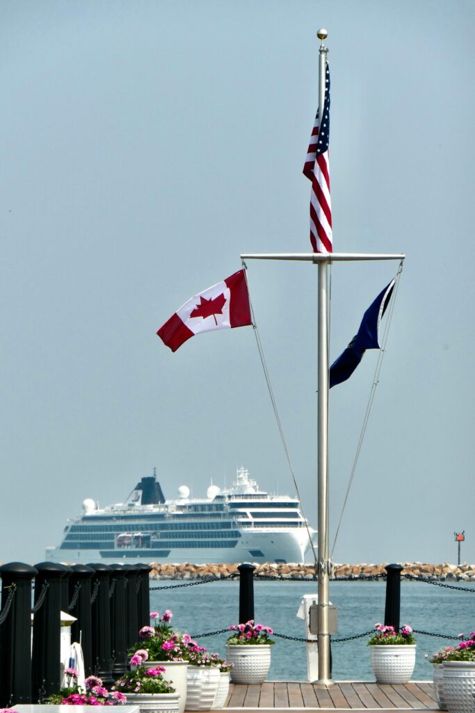 View of a cruise ship approaching Mackinac Island pier with American, Canadian, and local flags flying.