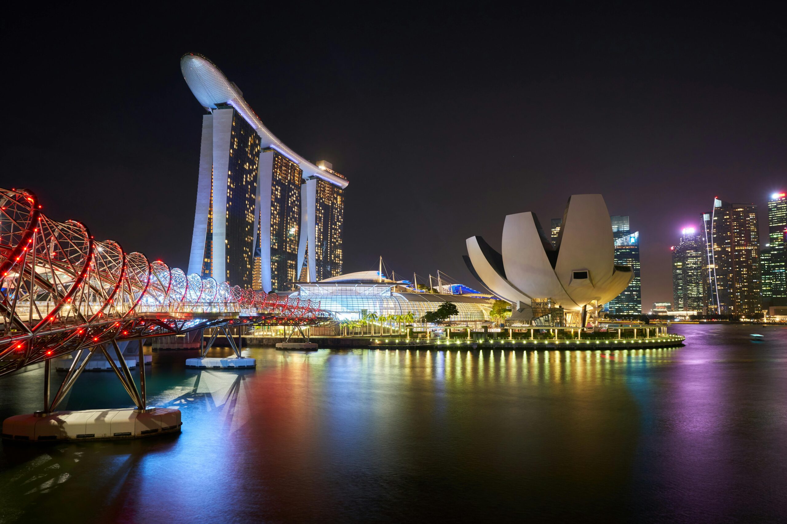 Stunning night view of Marina Bay Sands and Helix Bridge illuminated over water in Singapore.