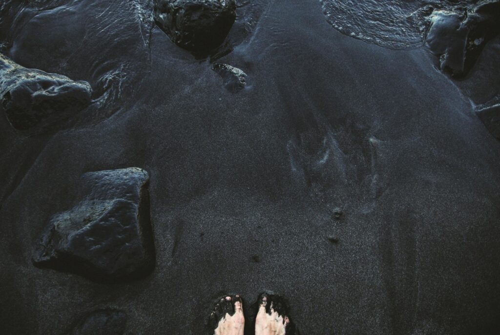 Feet touching the unique volcanic black sand beach in La Orotava, Spain.