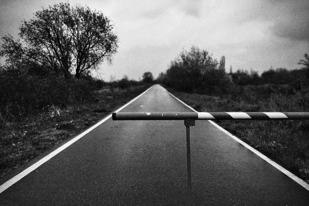 A lonely rural road blocked by a barrier under cloudy skies.