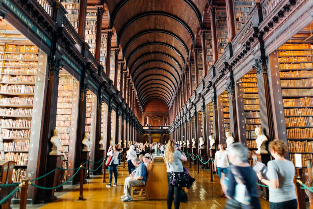 Visitors explore a grand library hallway with towering bookshelves in an iconic university.