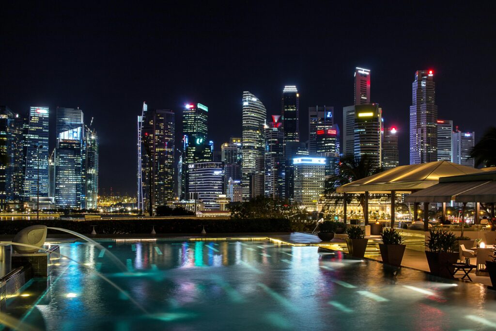 Vibrant night view of Singapore's illuminated skyline with a foreground infinity pool reflecting city lights.