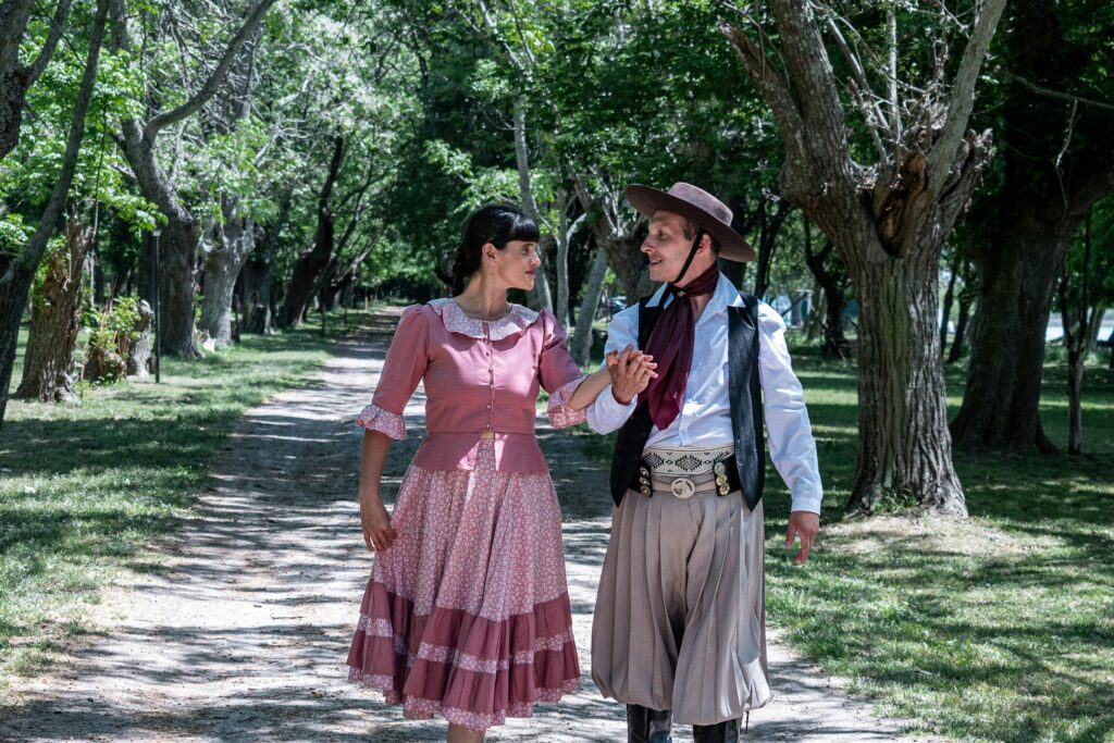 Couple in traditional gaucho attire dancing in a scenic park in Chascomús, Argentina.