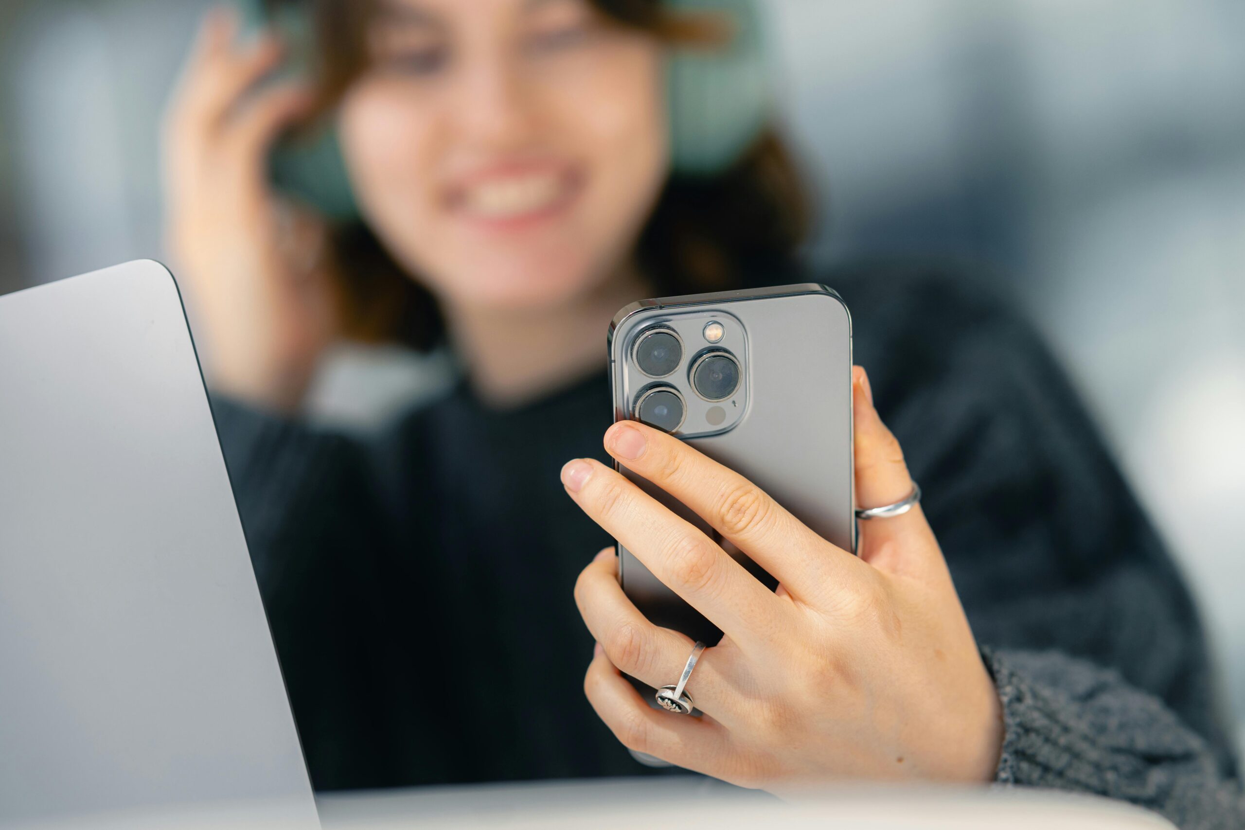 Smiling woman enjoys technology with smartphone, laptop, and headphones indoors.