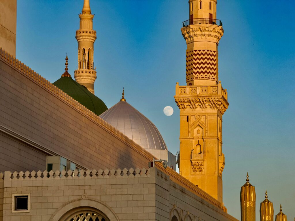 Stunning shot of the Prophet's Mosque minarets in Medina during dusk with a clear view of the moon.