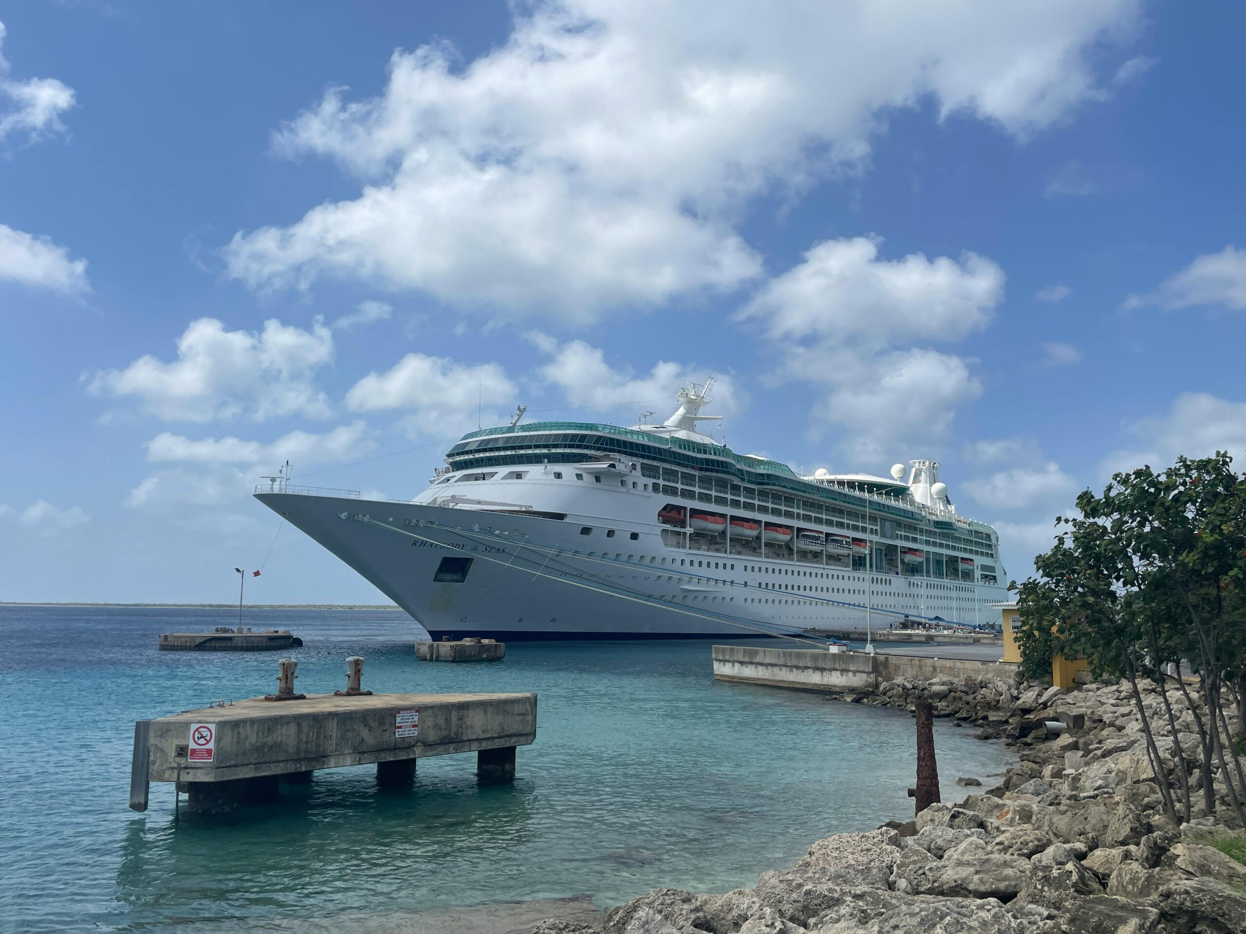 A luxurious cruise ship docked in a crystal clear tropical harbor, under a bright blue sky.