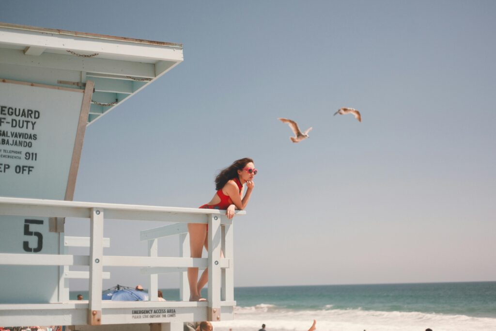 Stylish woman in red swimsuit posing at a beach lifeguard tower.