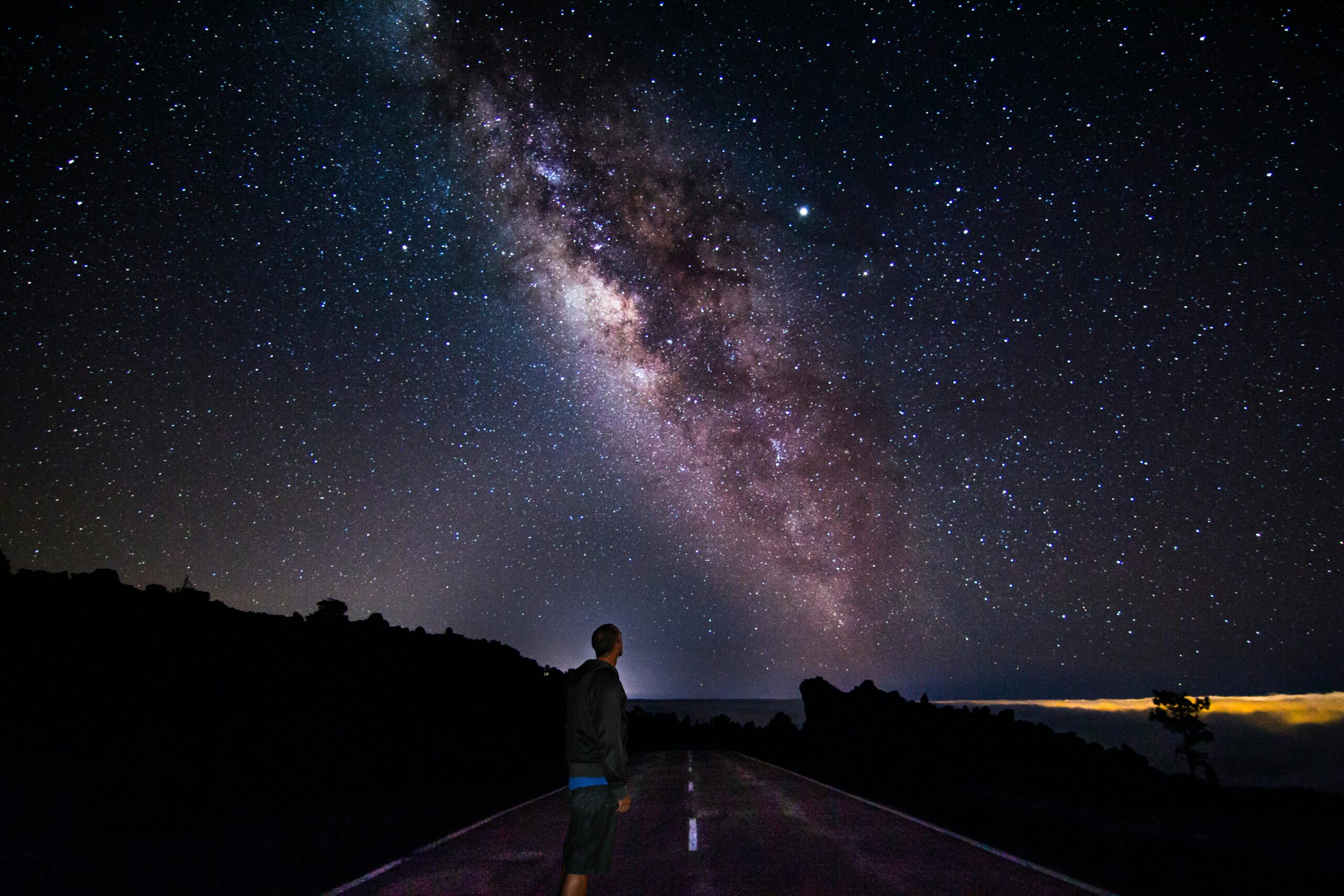 A lone figure gazes at the star-filled sky with the Milky Way over Santa Cruz de Tenerife.