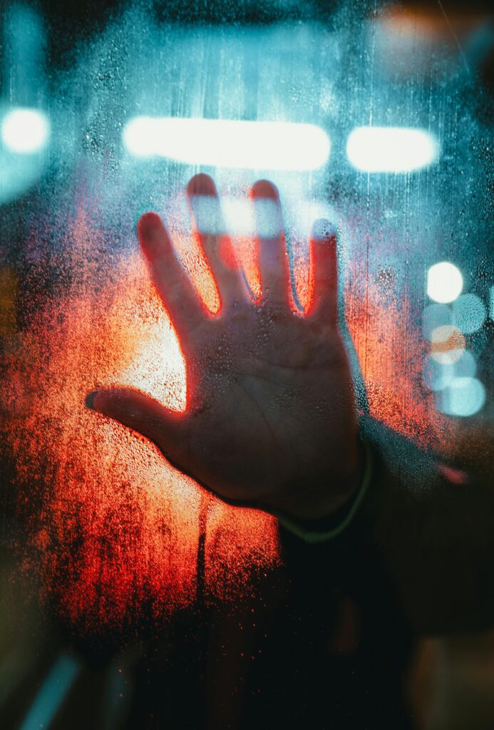 A dramatic depiction of a hand pressed against a foggy, illuminated window.