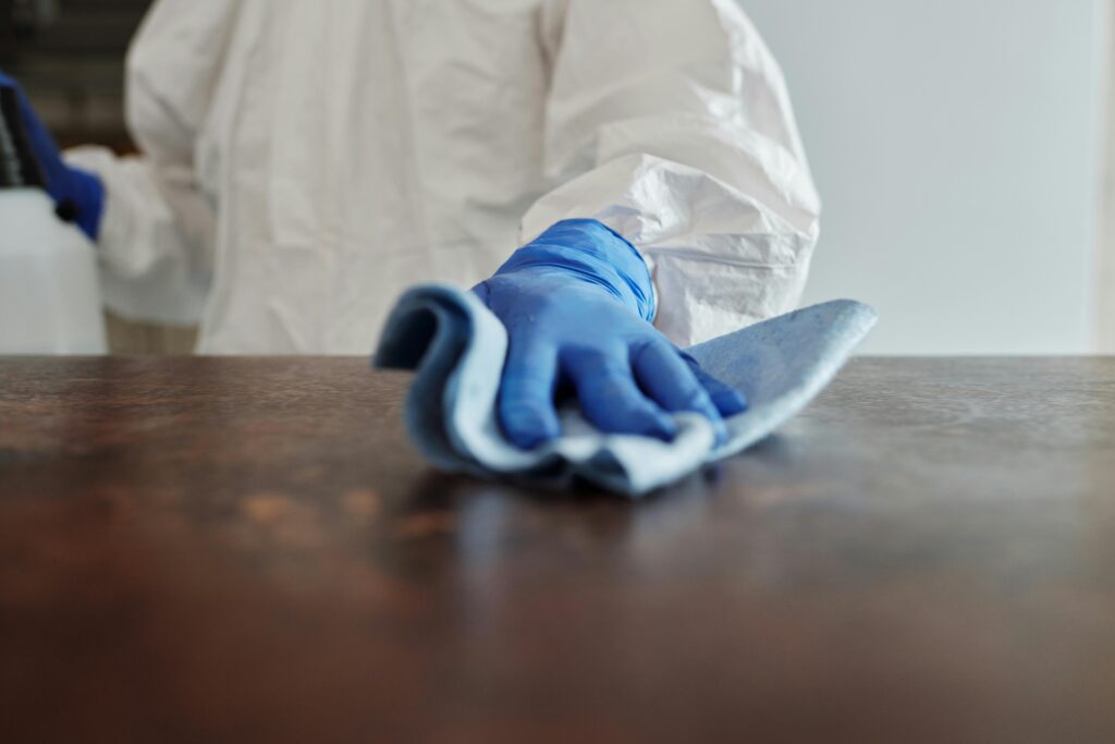 Person in protective suit using disinfectant on surface to ensure cleanliness and safety.