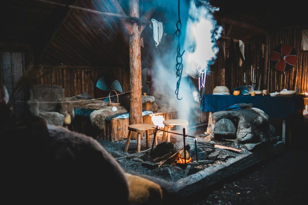 Burning bonfire inside of aged wooden house with bed and armchairs in Norstead Viking Village