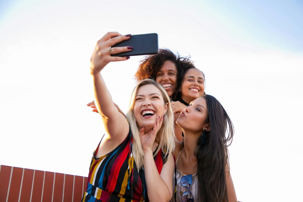 A joyful group of diverse women capturing a fun moment outdoors with a smartphone.