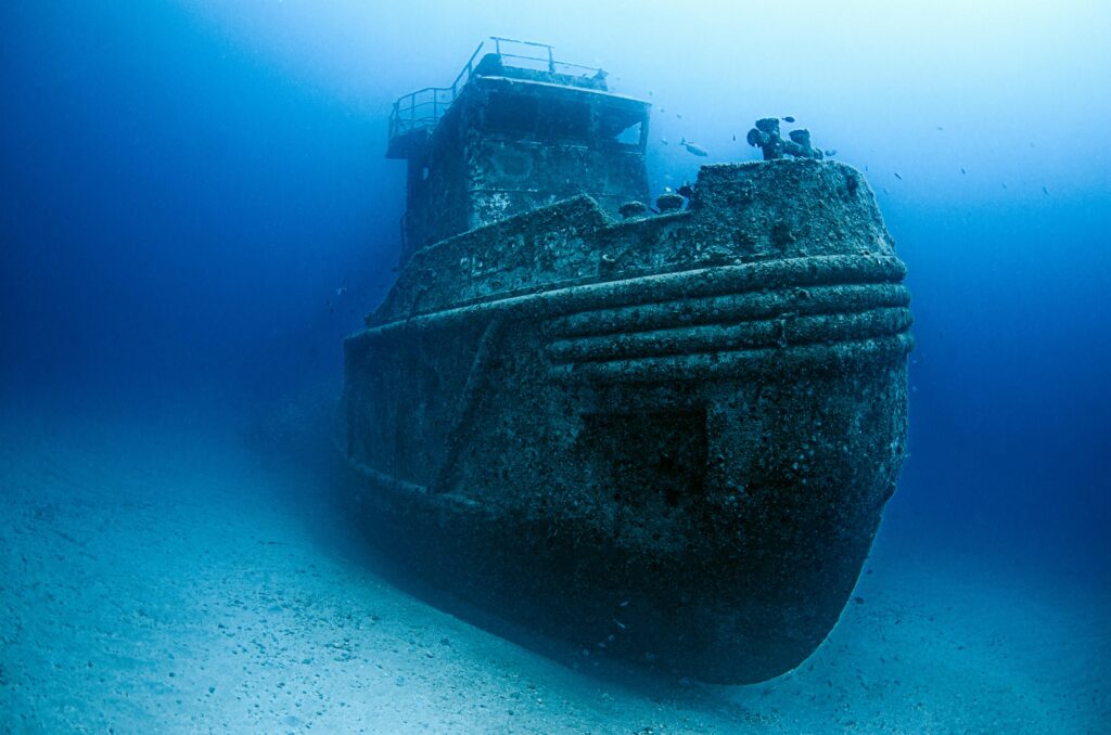 Explore the hauntingly beautiful underwater world of a sunken ship surrounded by marine life.