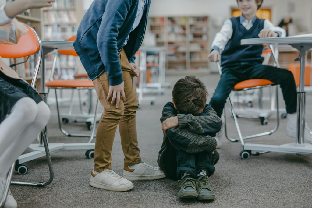 A young child sitting on the floor in a classroom facing bullying from peers.